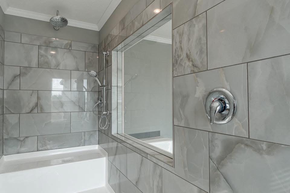 Modern shower with large gray marble tiles and a chrome showerhead. A built-in niche and sleek tub enhance the minimalist and clean aesthetic.