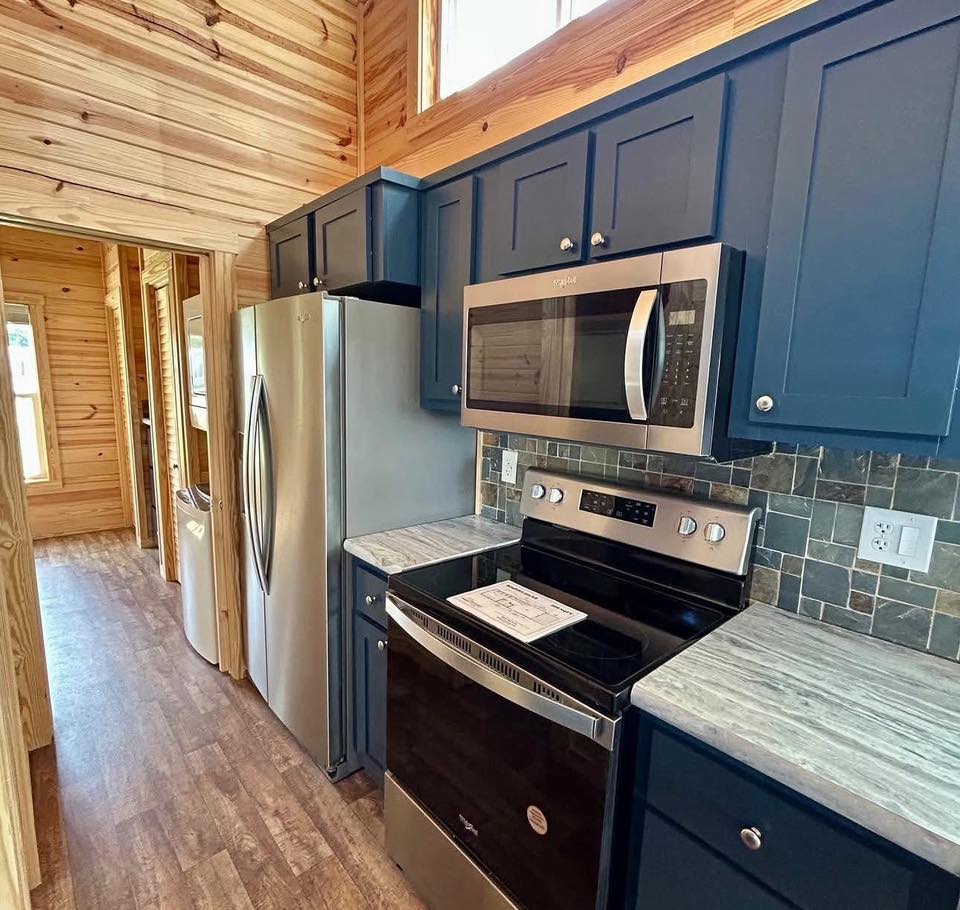Compact kitchen with dark blue cabinets, stainless steel appliances, and wood-paneled walls. The vibe is modern and cozy.