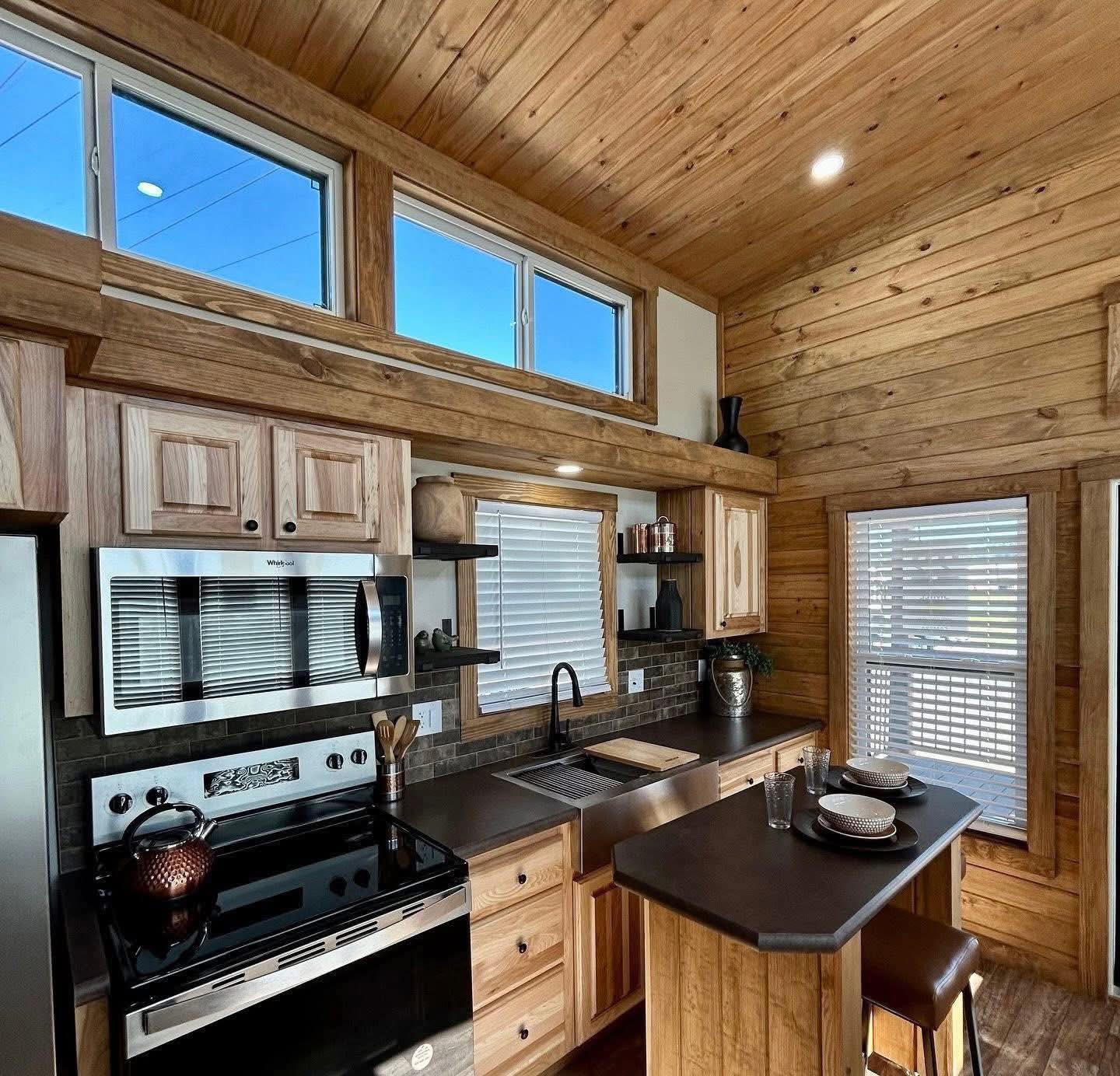 Cozy wooden kitchen with natural light. Features stainless steel appliances, dark countertops, bar stools, and high windows, creating a warm, inviting atmosphere.