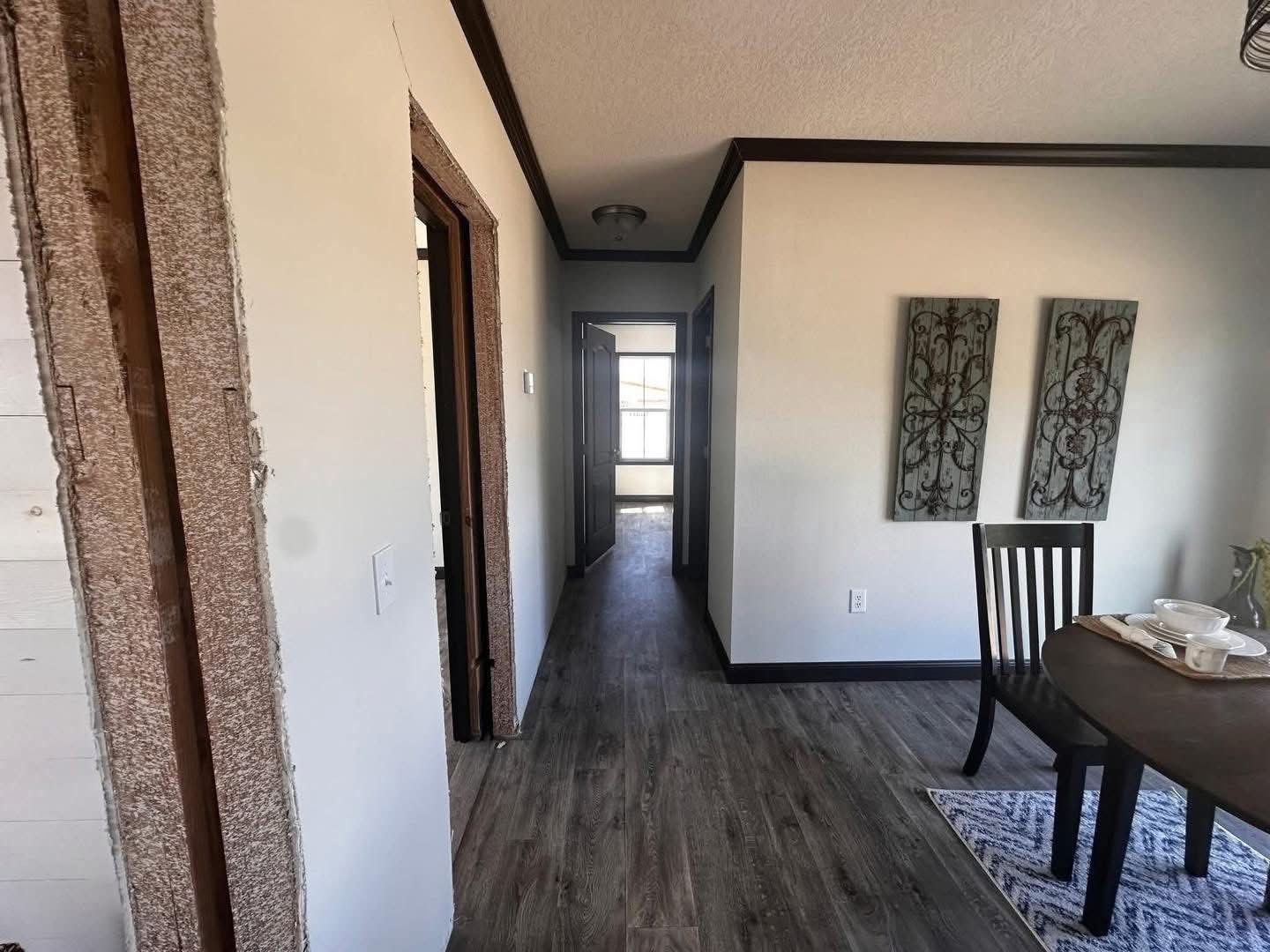 Hallway and dining area in a home with wood flooring and light walls. Two decorative metal panels hang on the wall. A table with place settings is visible.