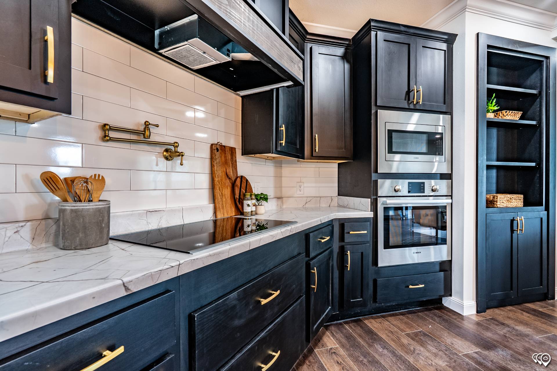Stylish kitchen with dark cabinets, brass handles, marble countertops, white subway tiles, and stainless steel oven and microwave. Cozy, modern vibe.
