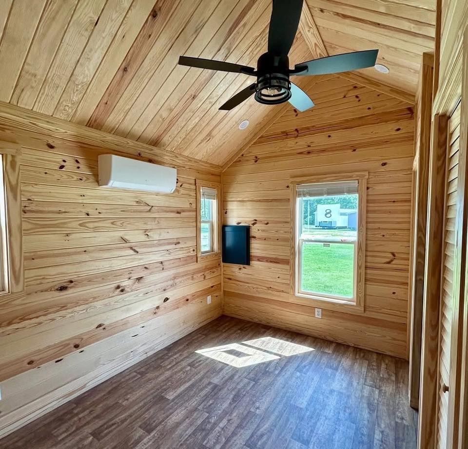Wood-paneled room with a vaulted ceiling and fan. Sunlight streams through large windows, highlighting the warm, natural tones and serene ambiance.
