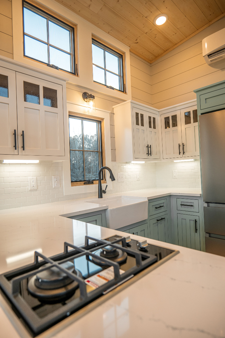 Modern kitchen with wood-paneled ceiling, white cabinets, and a sleek black stove on marble countertops. Sunlit from large windows, it feels bright and airy.