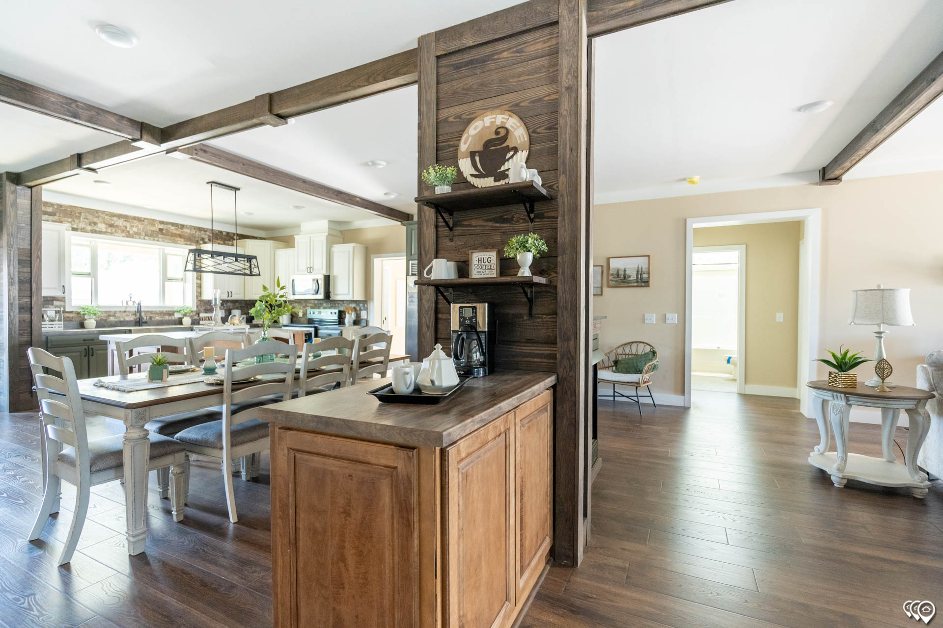 Open-concept kitchen and dining area with rustic wood beams, light wood floors, and farmhouse decor. A welcoming, cozy atmosphere prevails.