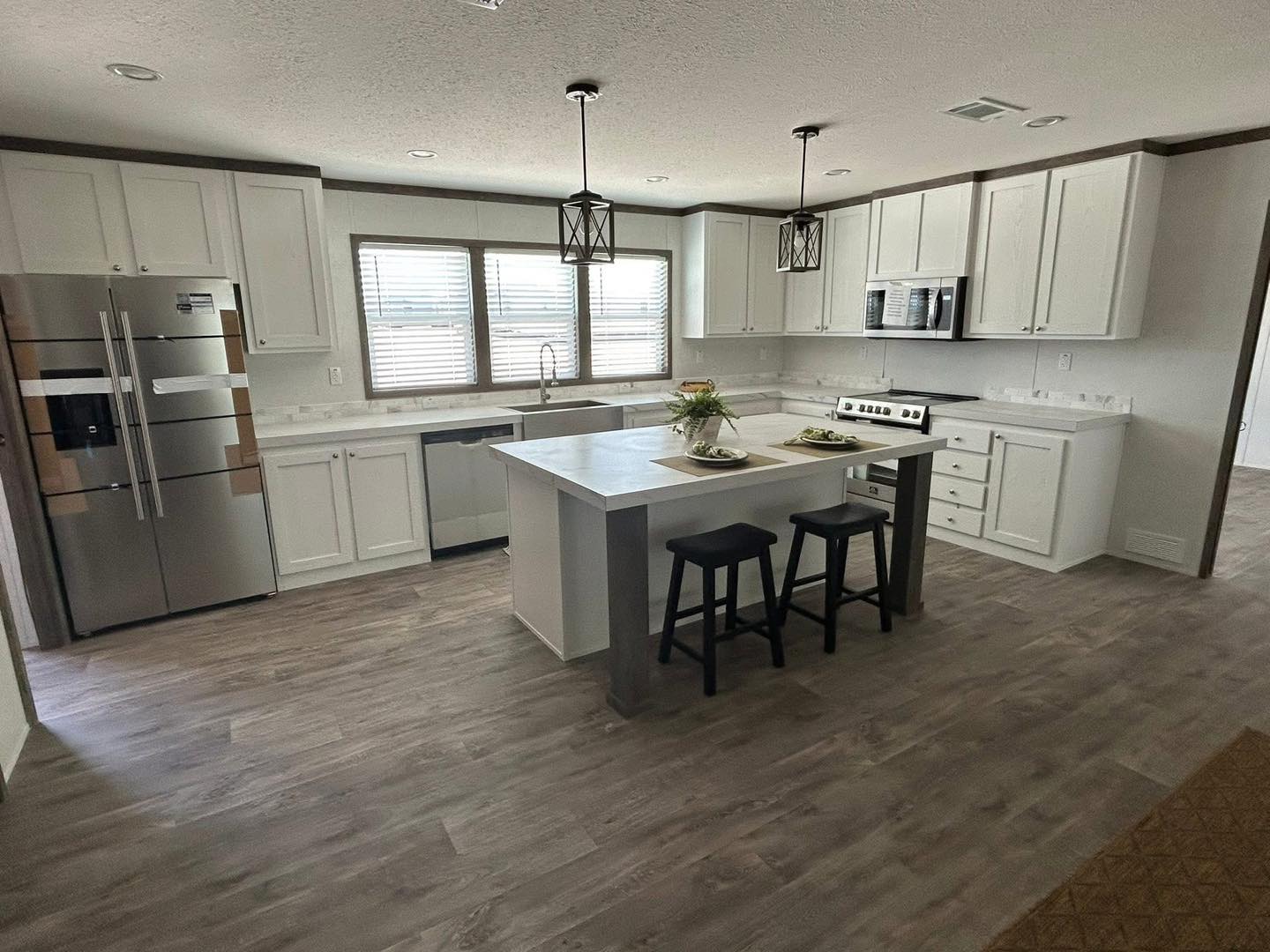 Modern kitchen with sleek white cabinets, a large island with two stools, stainless steel appliances, and pendant lights. Bright and inviting space.