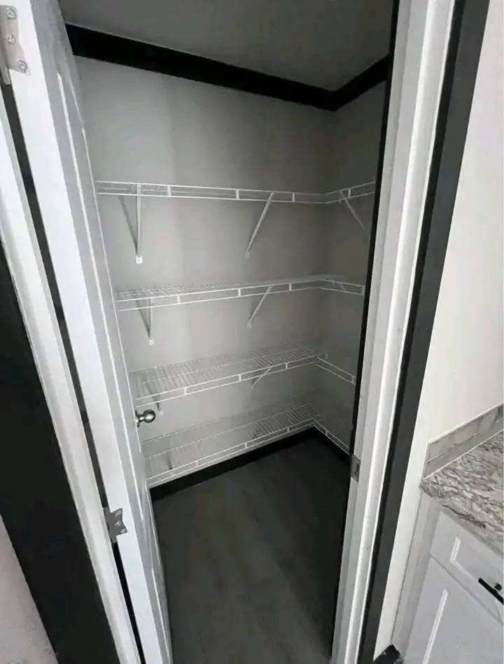 A small, empty pantry with white wire shelves on gray walls. Wooden flooring and a white door add a minimalist feel to the space.