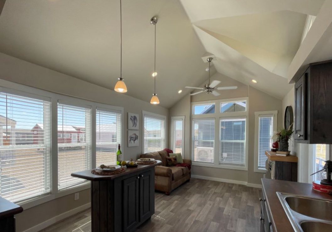 Bright living room with high ceilings, natural light from large windows, a cozy sofa, kitchen island, and modern pendant lights create an inviting atmosphere.
