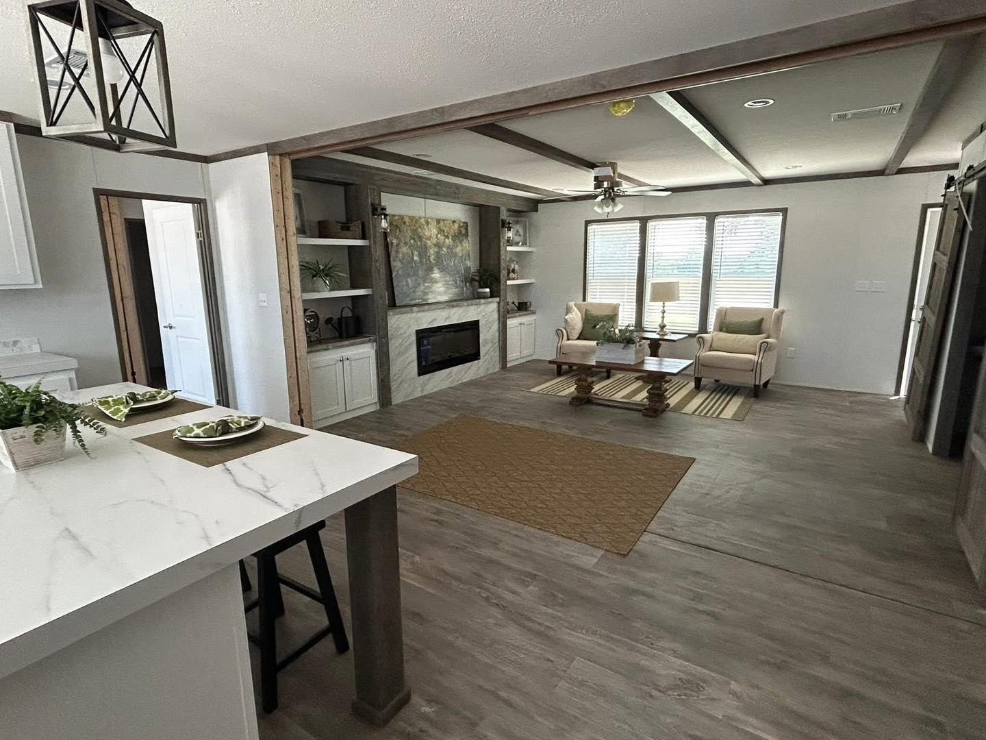 Modern living room with a cozy vibe, featuring wood floors, a fireplace in a wall unit, and natural light streaming through large windows. Neutral tones.