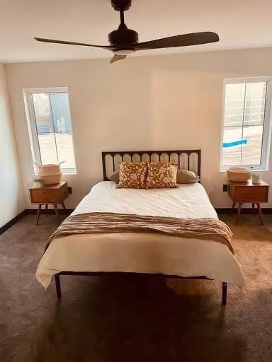A cozy bedroom with a neatly made bed, featuring patterned pillows and a striped throw. Flanked by wooden nightstands, under a modern ceiling fan. Minimalist and serene.