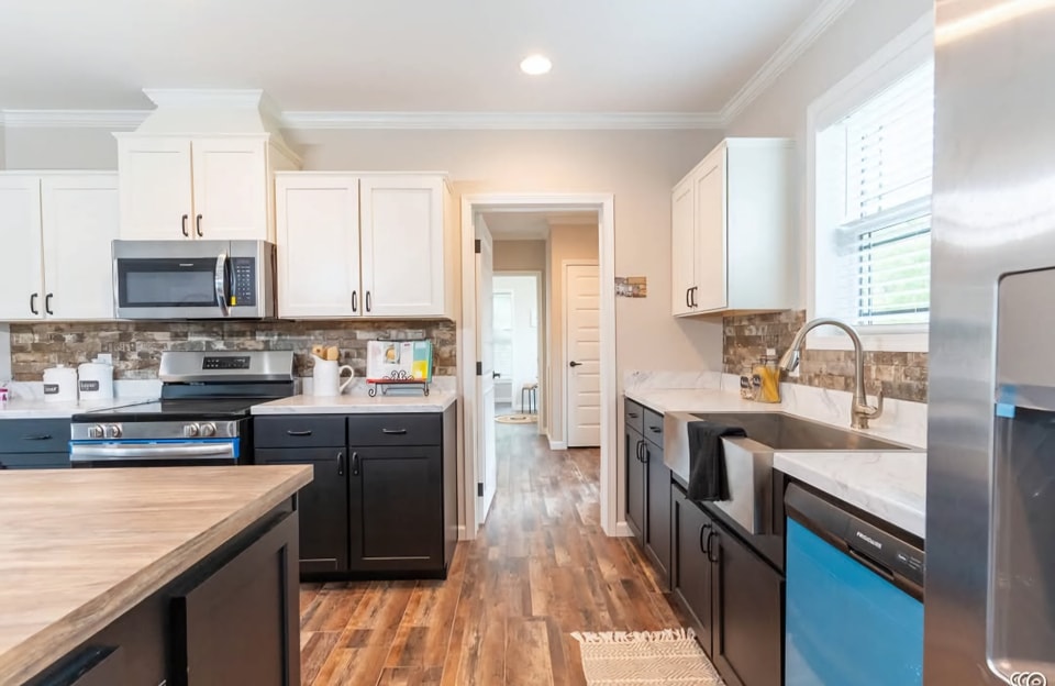 Bright, modern kitchen with white and black cabinetry, stainless steel appliances, hardwood floors, and a white farmhouse sink. Warm, inviting atmosphere.