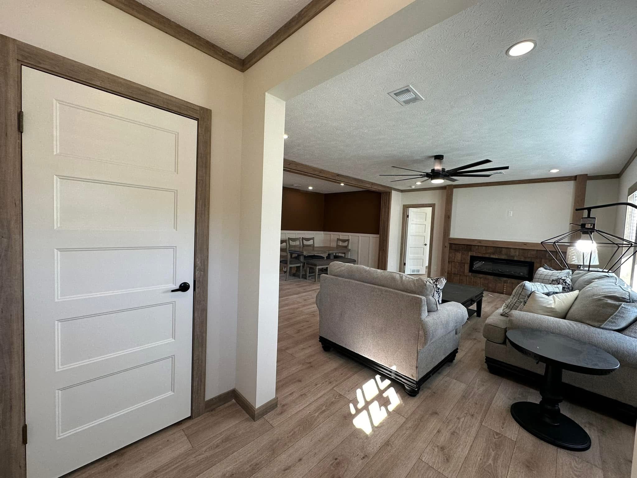 Comfortable living room with light wood flooring, two gray sofas, and a modern ceiling fan. Adjacent dining room visible; natural light streams in.