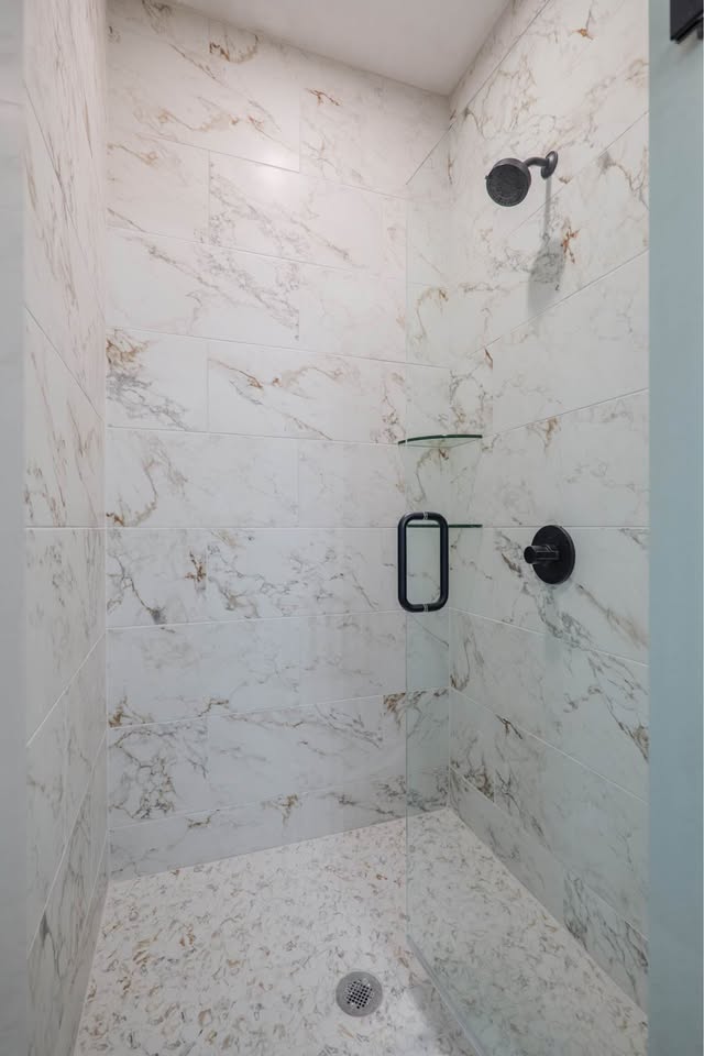 Modern shower with white marble tiles featuring gold veining, a black showerhead and handle, and a sleek glass door conveying a clean, elegant feel.