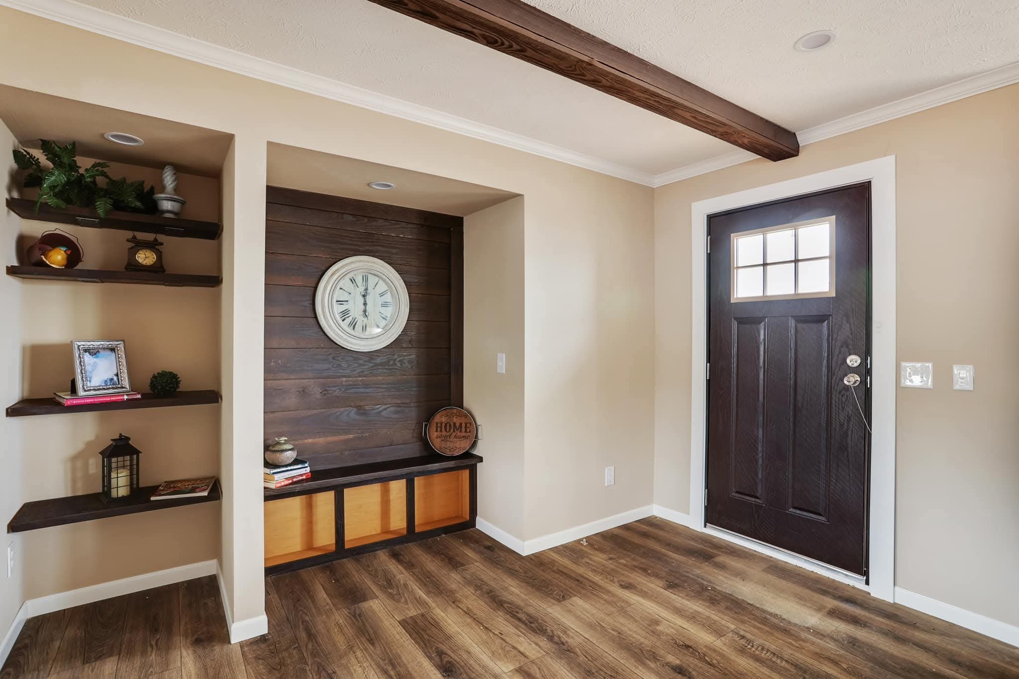 A cozy entryway with wood flooring features a dark wooden door and a recessed nook with rustic shelves. A vintage clock and decor create a welcoming tone.