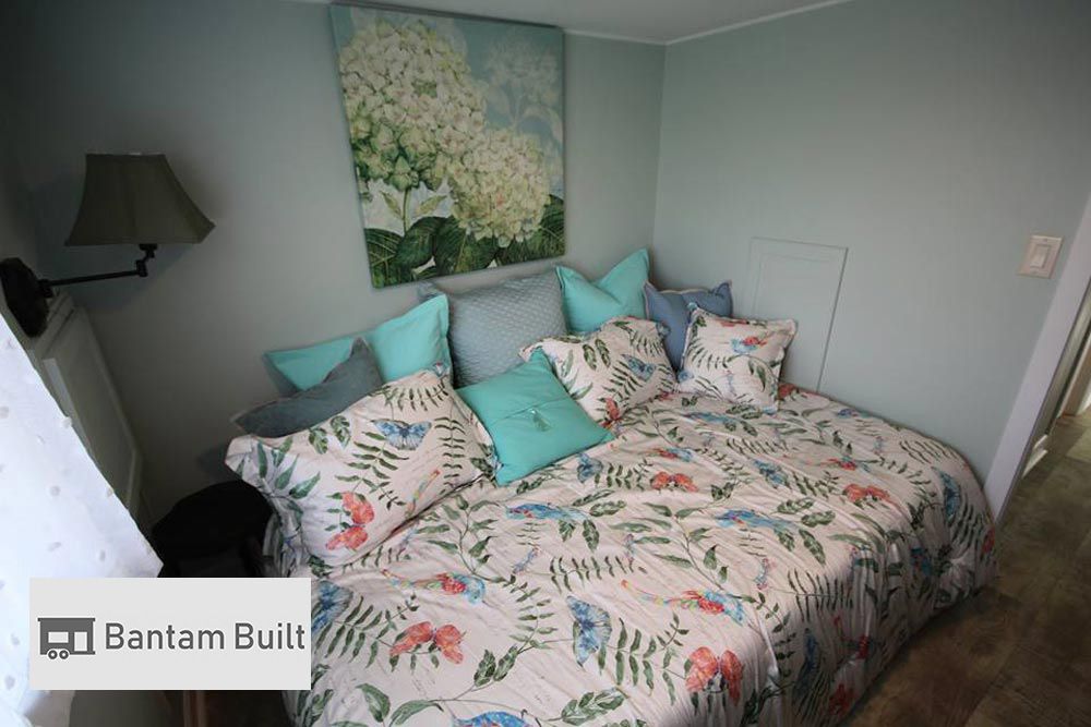 Cozy bedroom with a floral-patterned bedspread, pastel pillows, and a hydrangea painting on blue walls. Soft, calming, and inviting atmosphere.