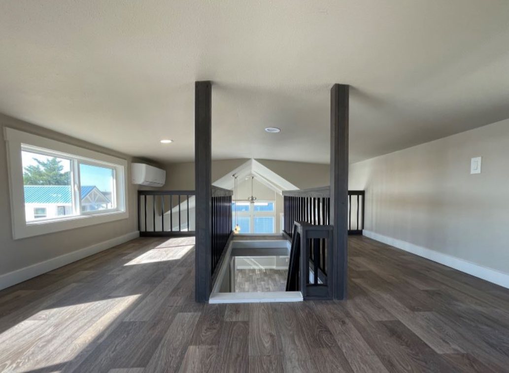 Attic with wooden flooring, large window, and a railing overlooking a lower level. Soft lighting and a modern, airy atmosphere.