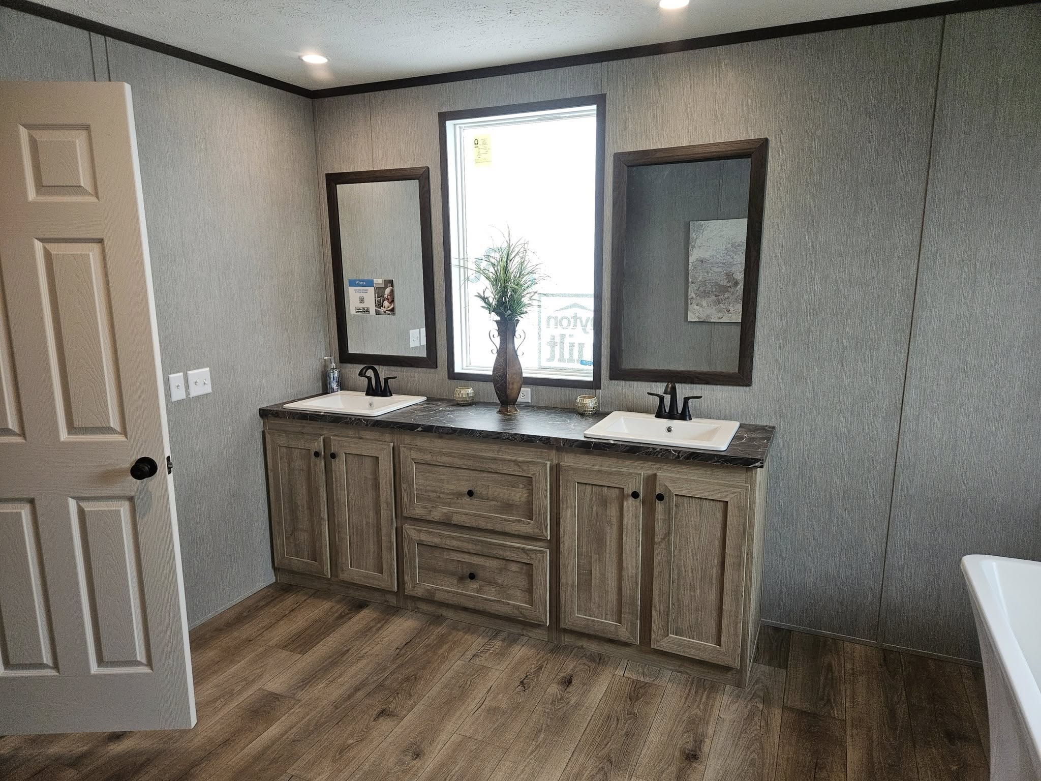 Modern bathroom with dual sinks, wooden cabinetry, and two mirrors. A small plant sits between the sinks. The space feels clean and elegant.