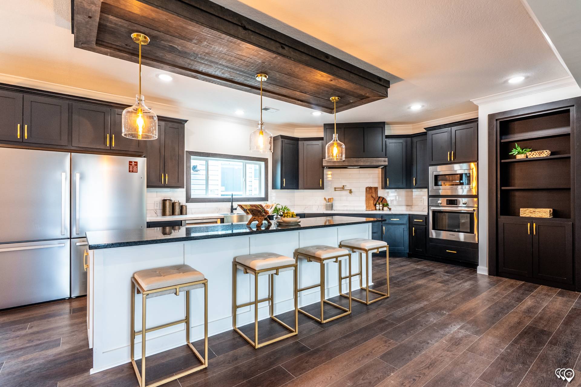 Modern kitchen with dark wood cabinets, stainless steel appliances, and a large island. Three pendant lights hang above the island with four stools. The atmosphere is sleek and contemporary.