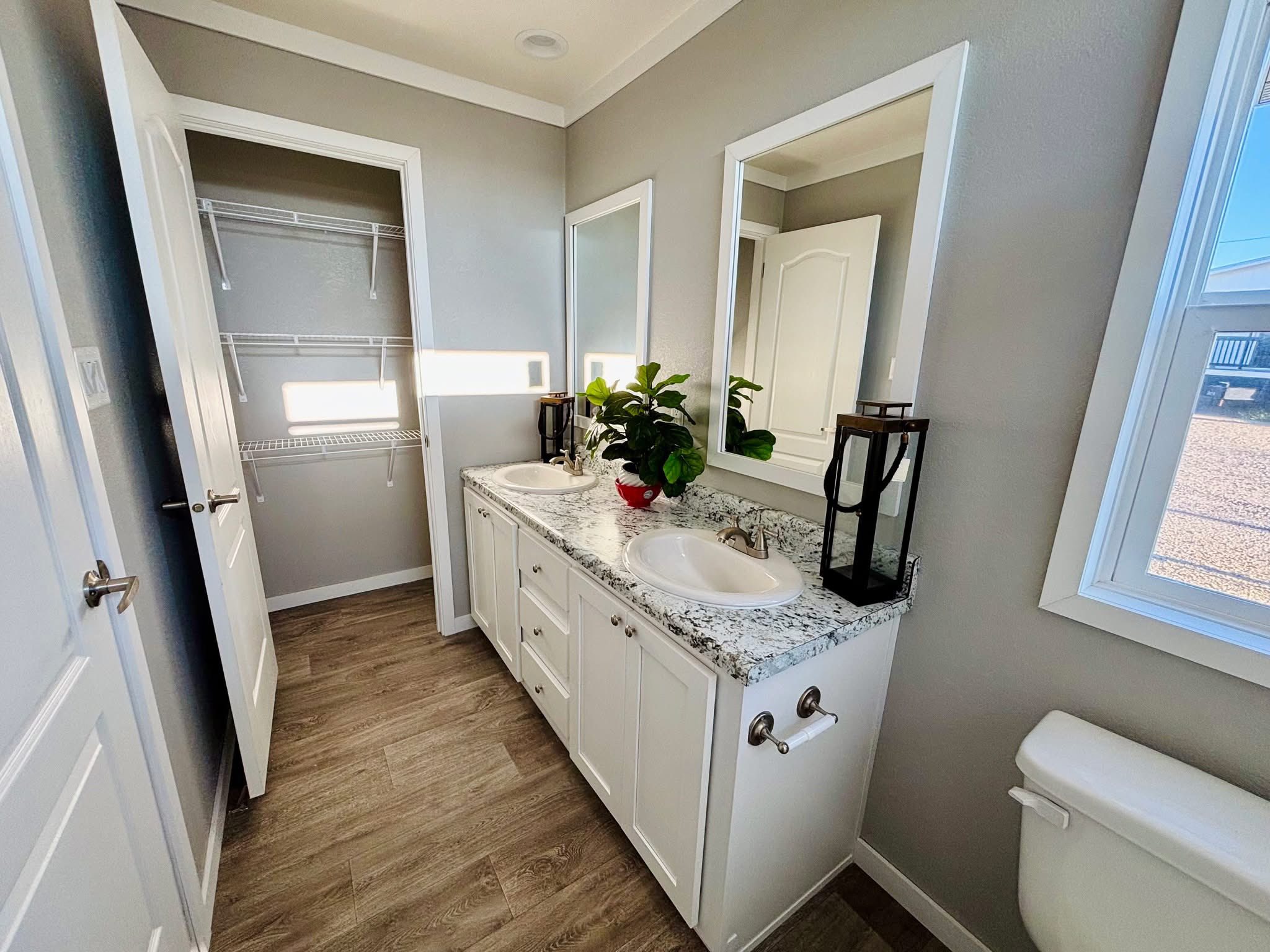 A compact, modern bathroom with a granite countertop sink, a white toilet, and a glass-enclosed shower. Natural light enters through two small windows.