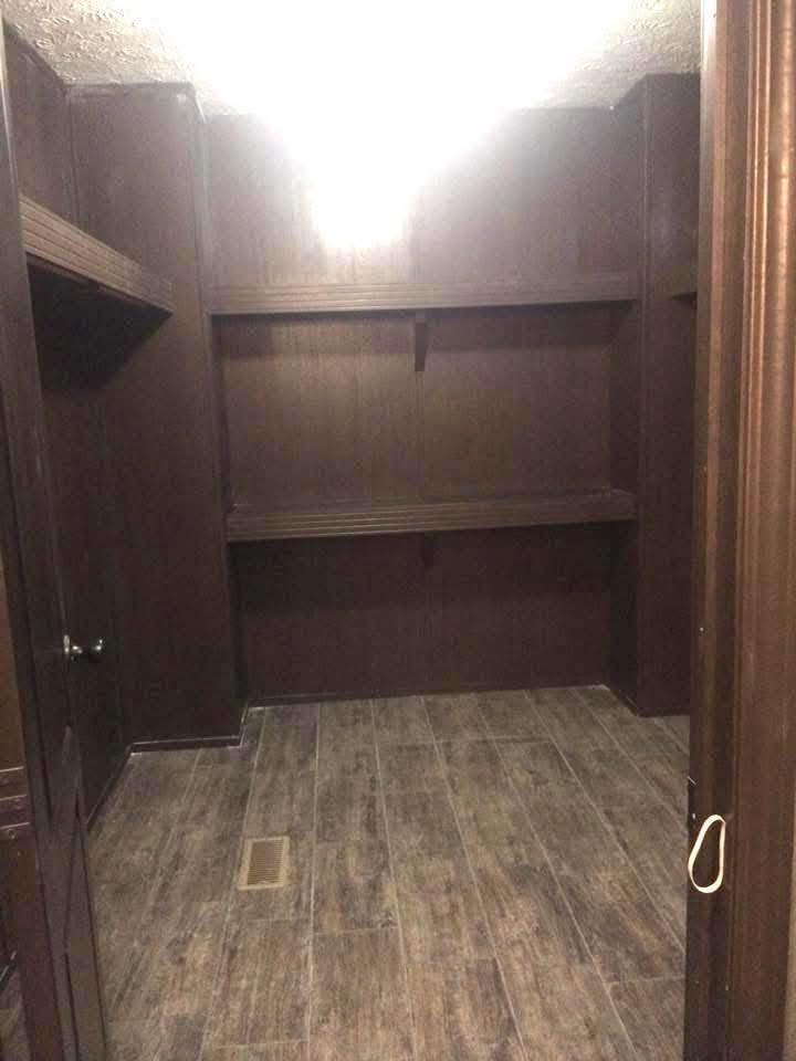 Dimly lit empty room with dark wooden walls and floor. Shelves line the back wall under a bright ceiling light, creating a stark contrast. Cozy yet sparse.