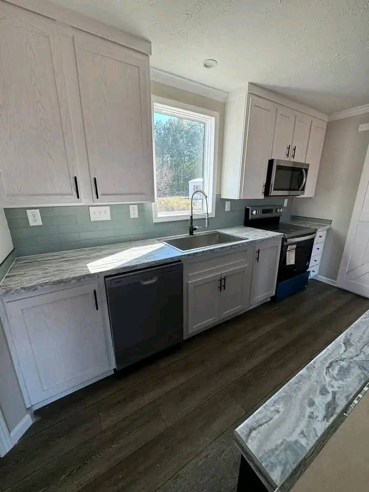 Modern kitchen with light wood cabinets, marble countertops, and stainless steel appliances. Sunlight streams through a window above the sink, creating a fresh and inviting atmosphere.