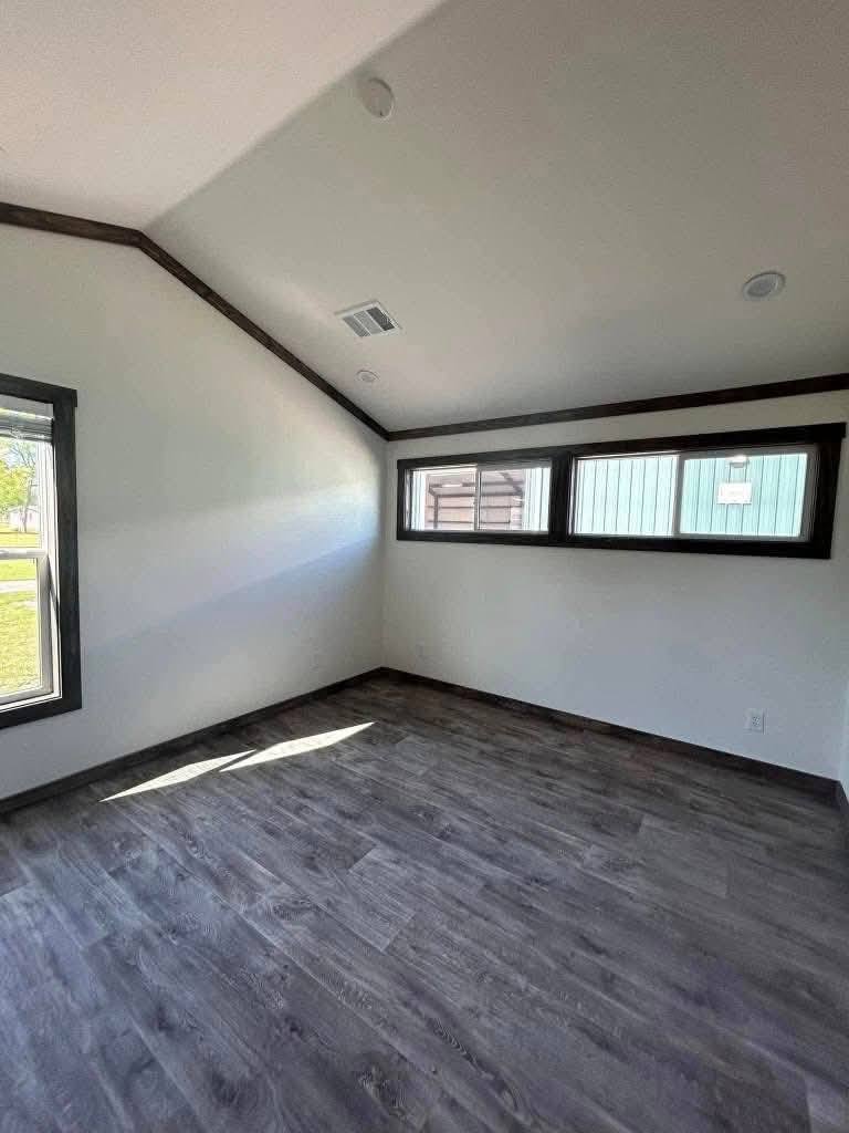 Small, empty room with slanted ceiling, dark wood floors, and white walls. Three narrow windows on the right. Bright and minimalist atmosphere.