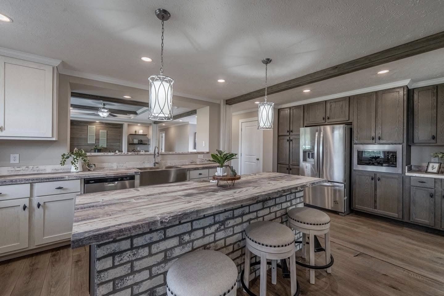 Modern kitchen with rustic charm, featuring a stone island, wooden cabinets, and stainless steel appliances. Two hanging lights add warmth.