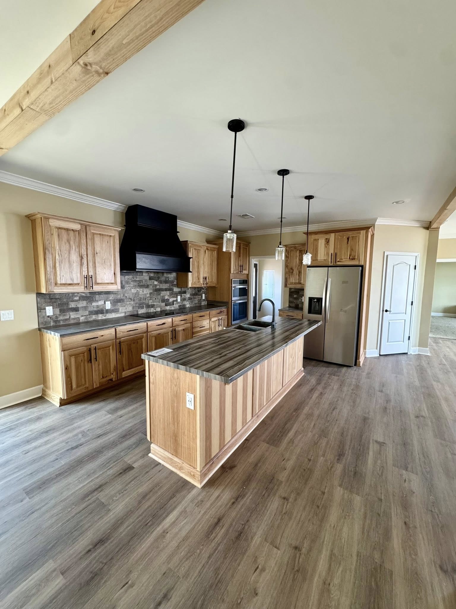 Spacious kitchen with wooden cabinets, central island, and a stainless steel fridge. Brick backsplash and warm lighting create a cozy, modern feel.