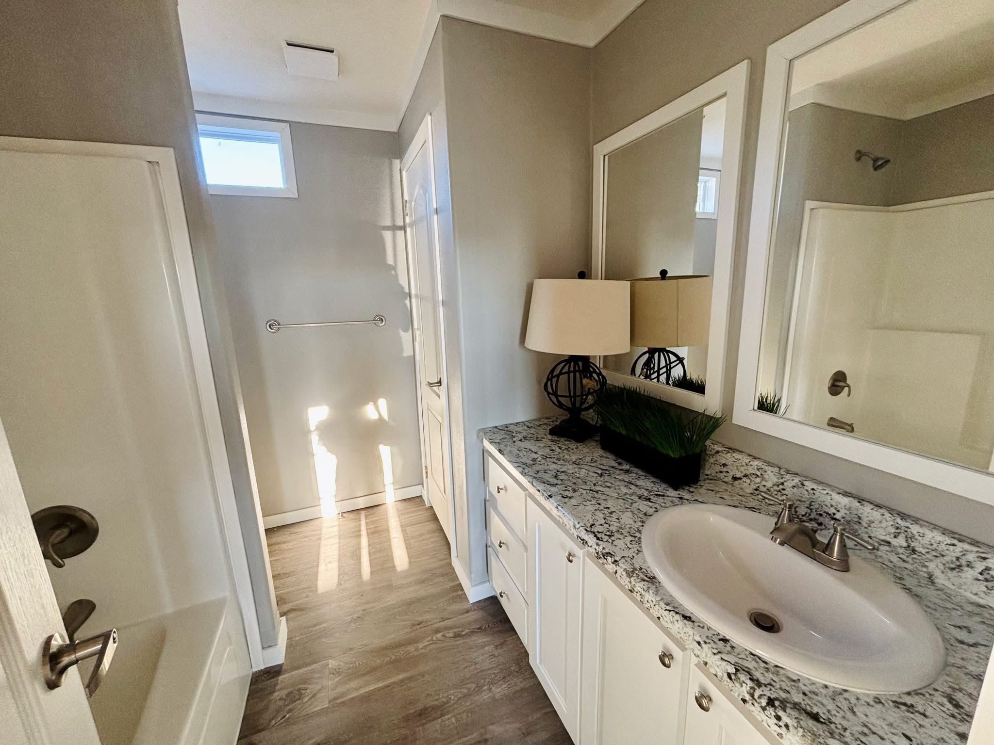 A small bathroom with gray walls, featuring a white shower stall on the left, a toilet under a high window, and wooden flooring, creating a clean look.