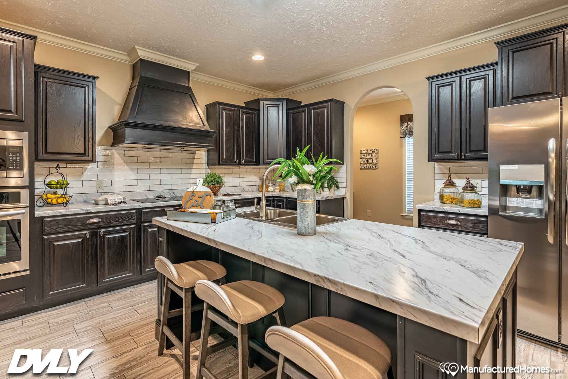 Modern kitchen with dark wood cabinets and stainless steel appliances. Features a marble island with seating, potted plants, and stylish decor.