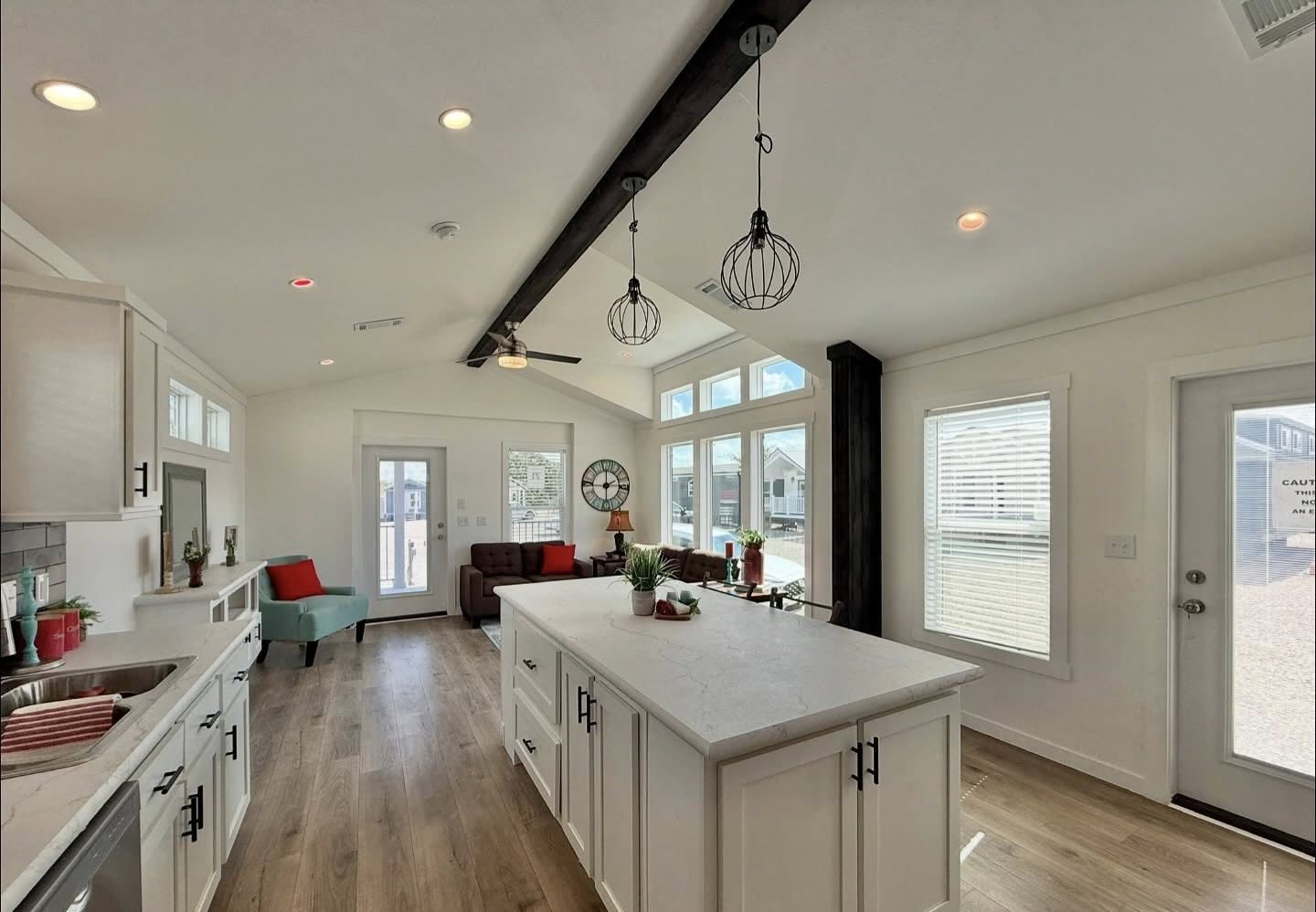 Spacious modern kitchen with white cabinets, large island, and wooden floors. Cozy seating area with red accents, high ceiling, and natural light.