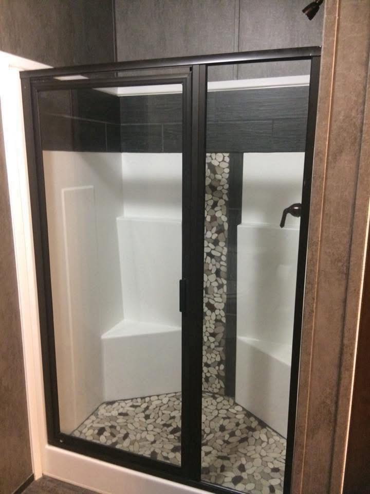 Modern shower with a black-framed glass door, featuring white walls, a pebble tile floor, and a built-in seat. Sleek and minimalist design.