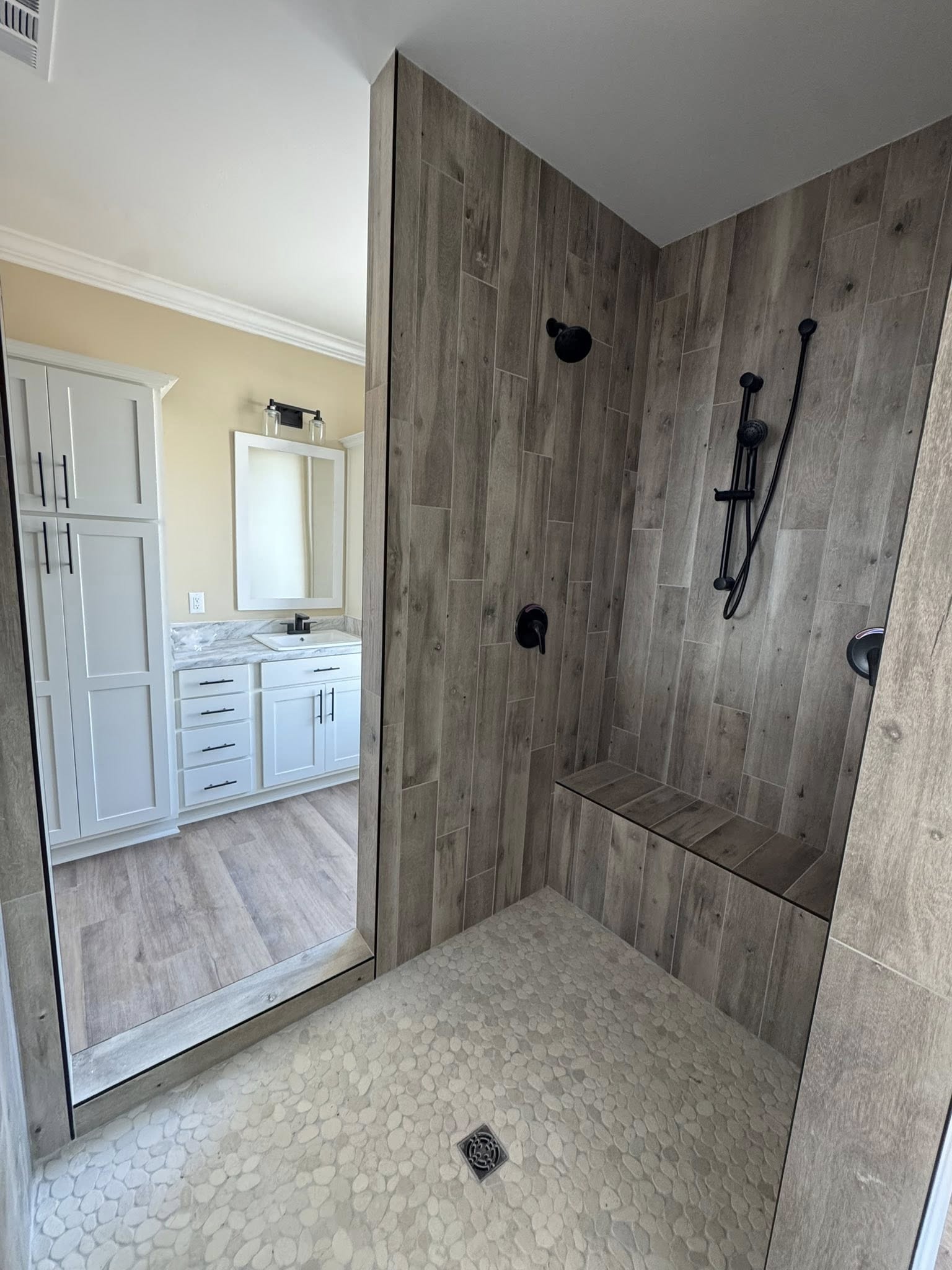Modern bathroom interior featuring a wood-paneled shower with black fixtures and a built-in bench. Adjacent is a white vanity with a marble countertop.