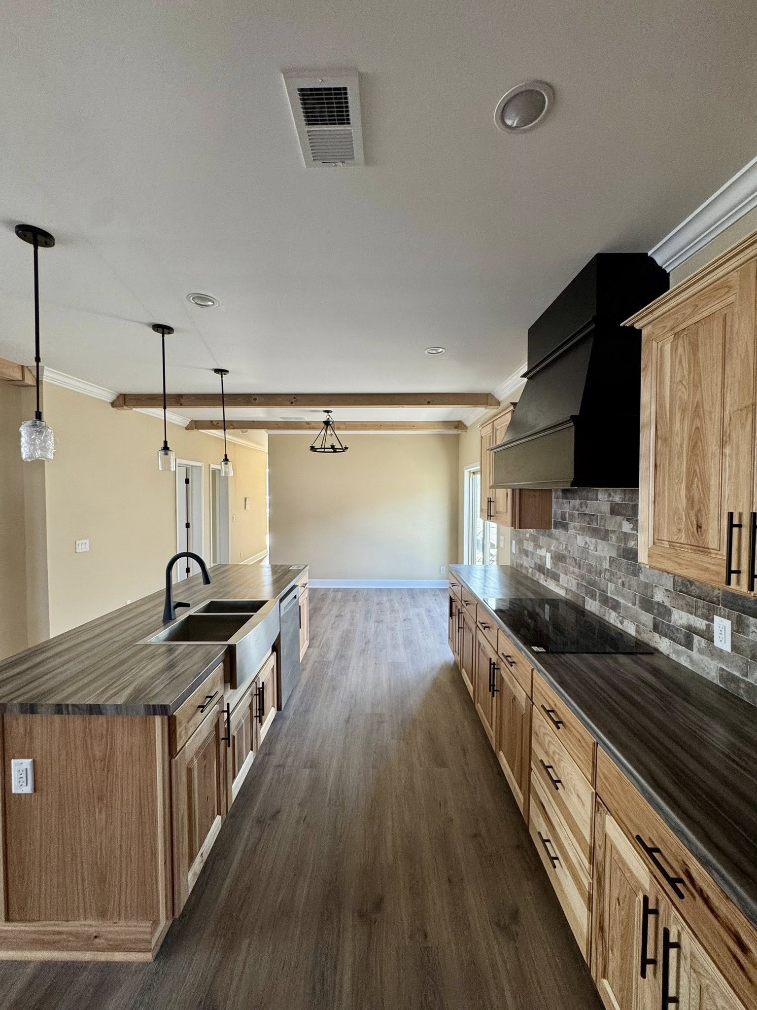 Spacious kitchen with light wood cabinets, dark countertops, and a central island. Modern pendant lights and rustic beams add a warm, elegant feel.