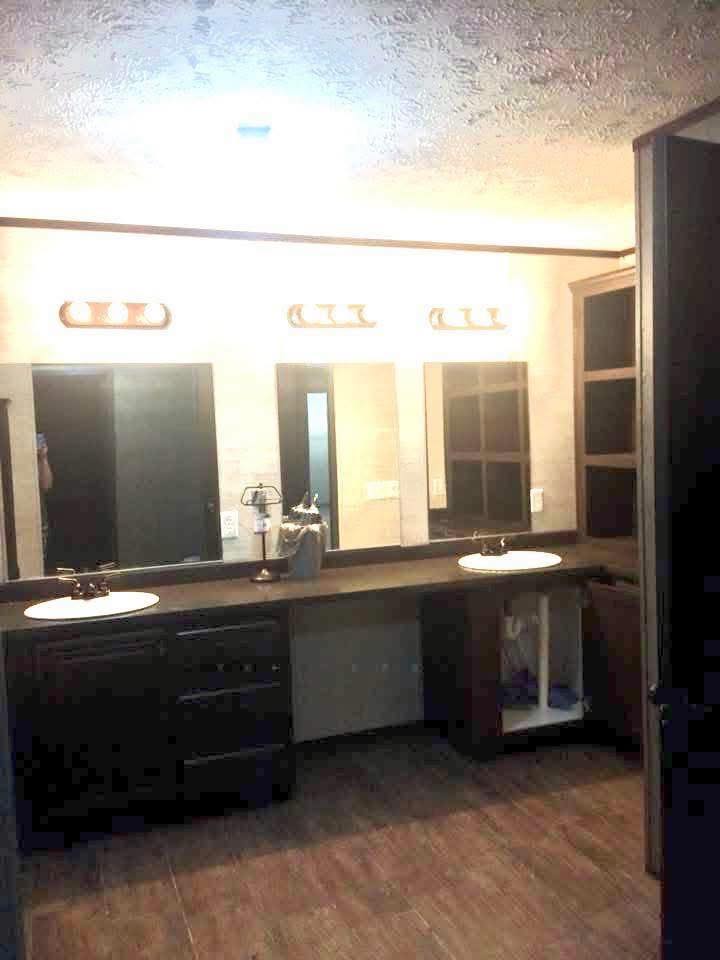 Modern bathroom with dual sinks, black countertops, and three mirrors. Warm lighting from stylish fixtures creates a welcoming atmosphere.