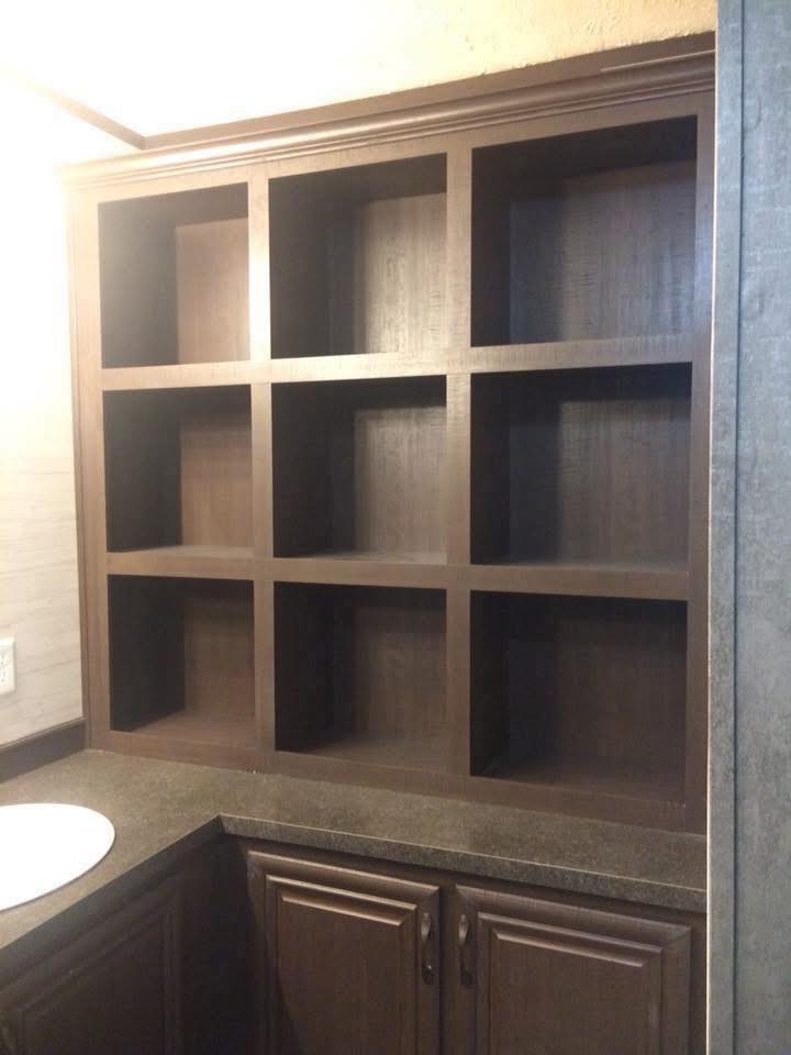 Dark wooden shelving unit with nine square compartments, set above a brown counter with cabinets and a white sink in the corner. The scene appears calm and organized.