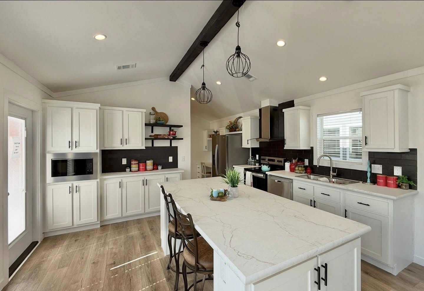 Modern kitchen with high ceilings, featuring a large white island, wooden stools, and pendant lights. White cabinets, stainless steel appliances, and wood accents convey a warm, inviting atmosphere.