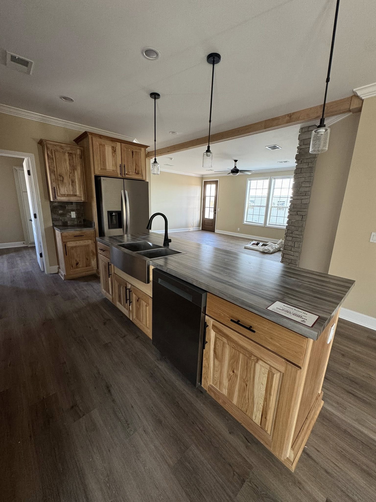 Modern kitchen with wood cabinets, gray countertops, and stainless steel appliances. Pendant lights hang above the island. Open concept with bright natural light.
