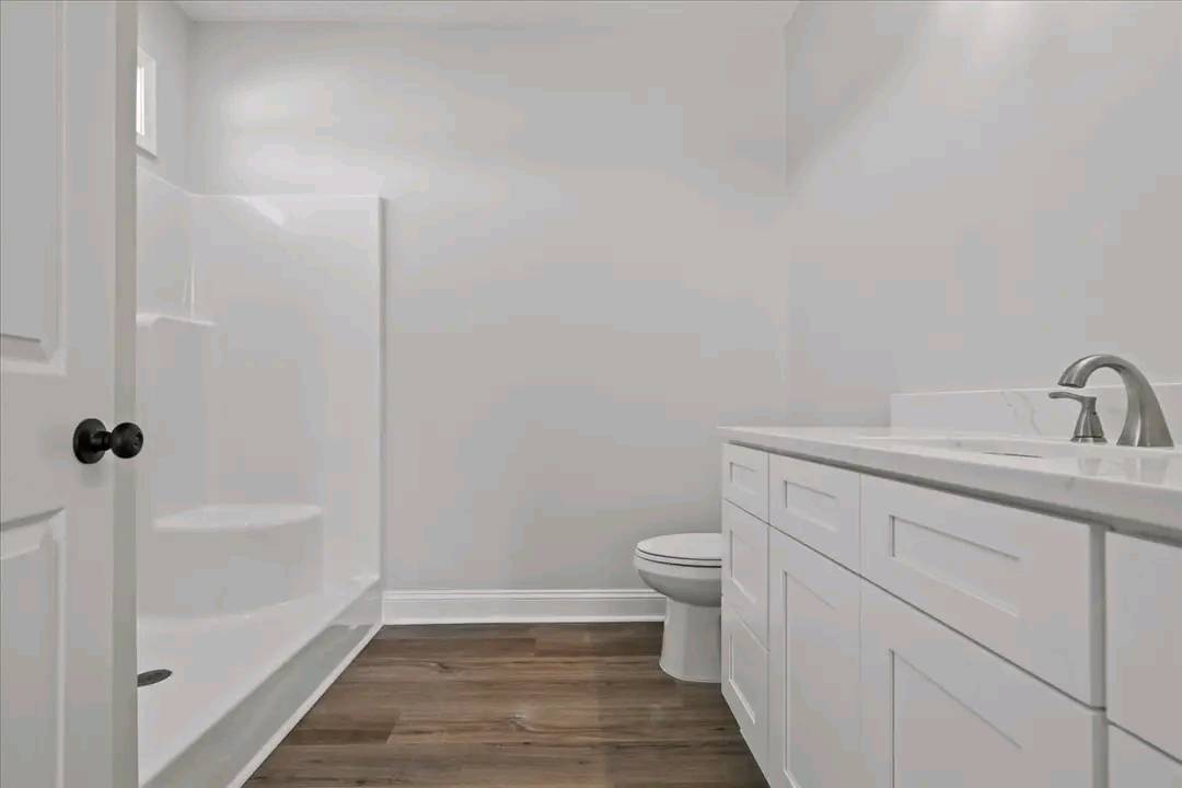 Modern bathroom with a sleek white vanity and faucet, a toilet, and a glass-enclosed shower. Warm wood flooring adds a touch of elegance.