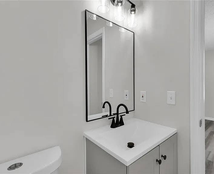 A modern bathroom features a sleek black faucet on a white vanity with a large rectangular mirror. Soft gray walls create a clean, minimalist look.