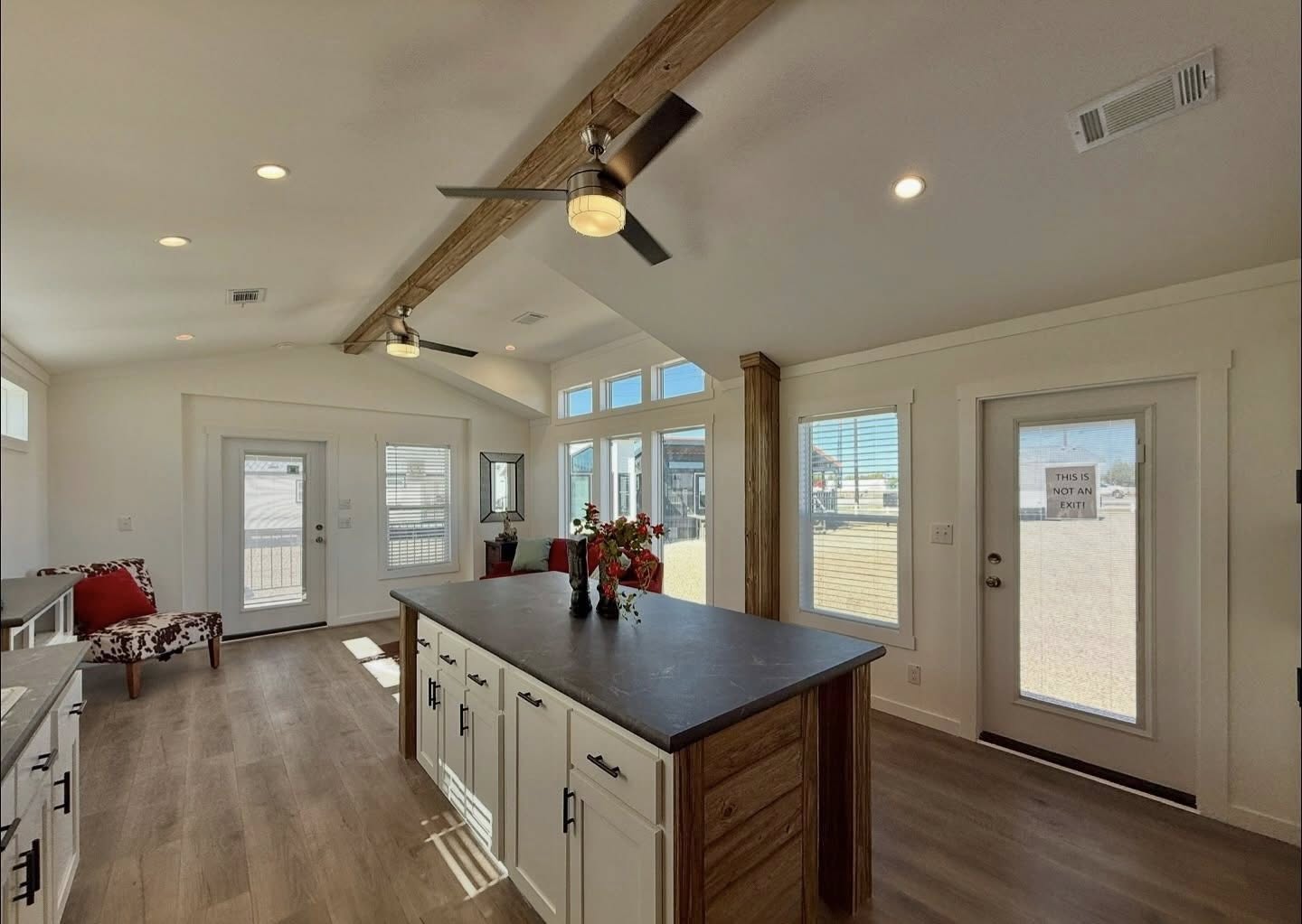 Spacious modern kitchen with a large island, wooden beams, and ceiling fans. Bright natural light fills the room through multiple windows, creating a warm and inviting atmosphere.