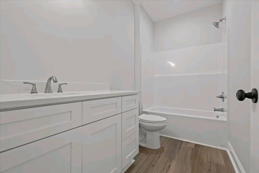 A modern bathroom with white cabinets, dual sinks, and chrome faucets. A bathtub and shower combo is on the right. The floor is wood, creating a clean and fresh atmosphere.