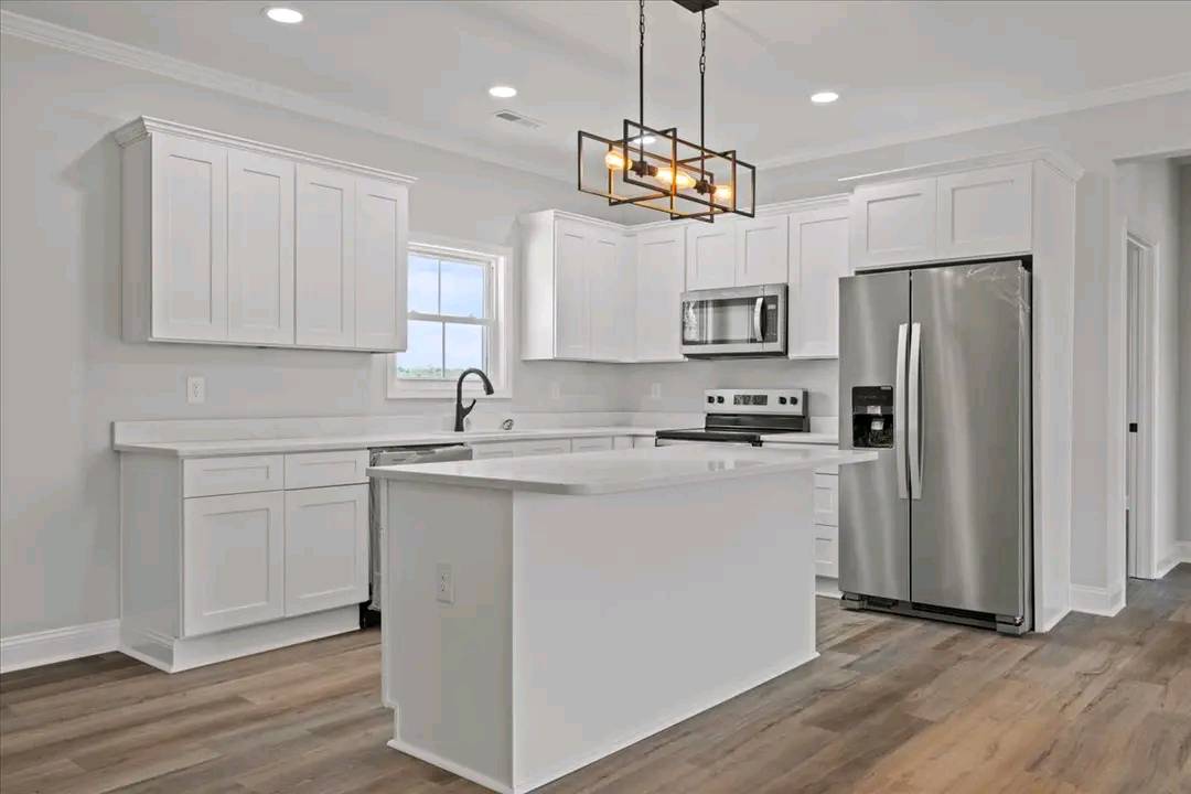Sleek kitchen with white cabinetry, stainless steel appliances, and a central island. Modern pendant light, wooden floor, and a bright ambiance.
