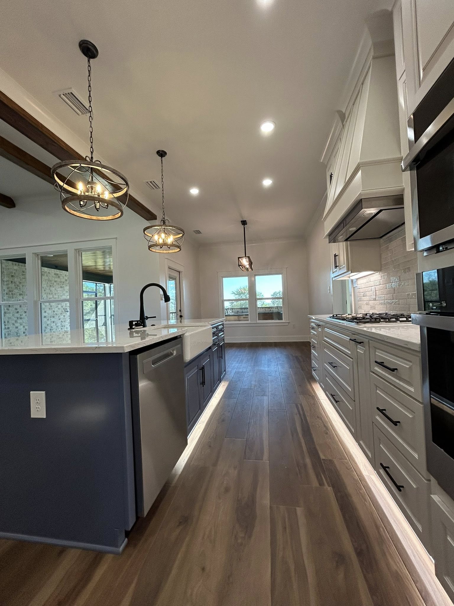 Spacious modern kitchen with wood floor, white cabinets, and a blue island. Pendant lights and a large window create a bright, inviting atmosphere.