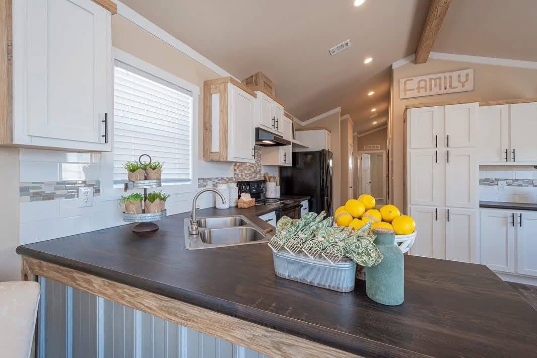 A cozy kitchen with white cabinets, wooden accents, and a dark countertop. Lemons and a rustic basket are on the counter, creating a warm, inviting atmosphere.