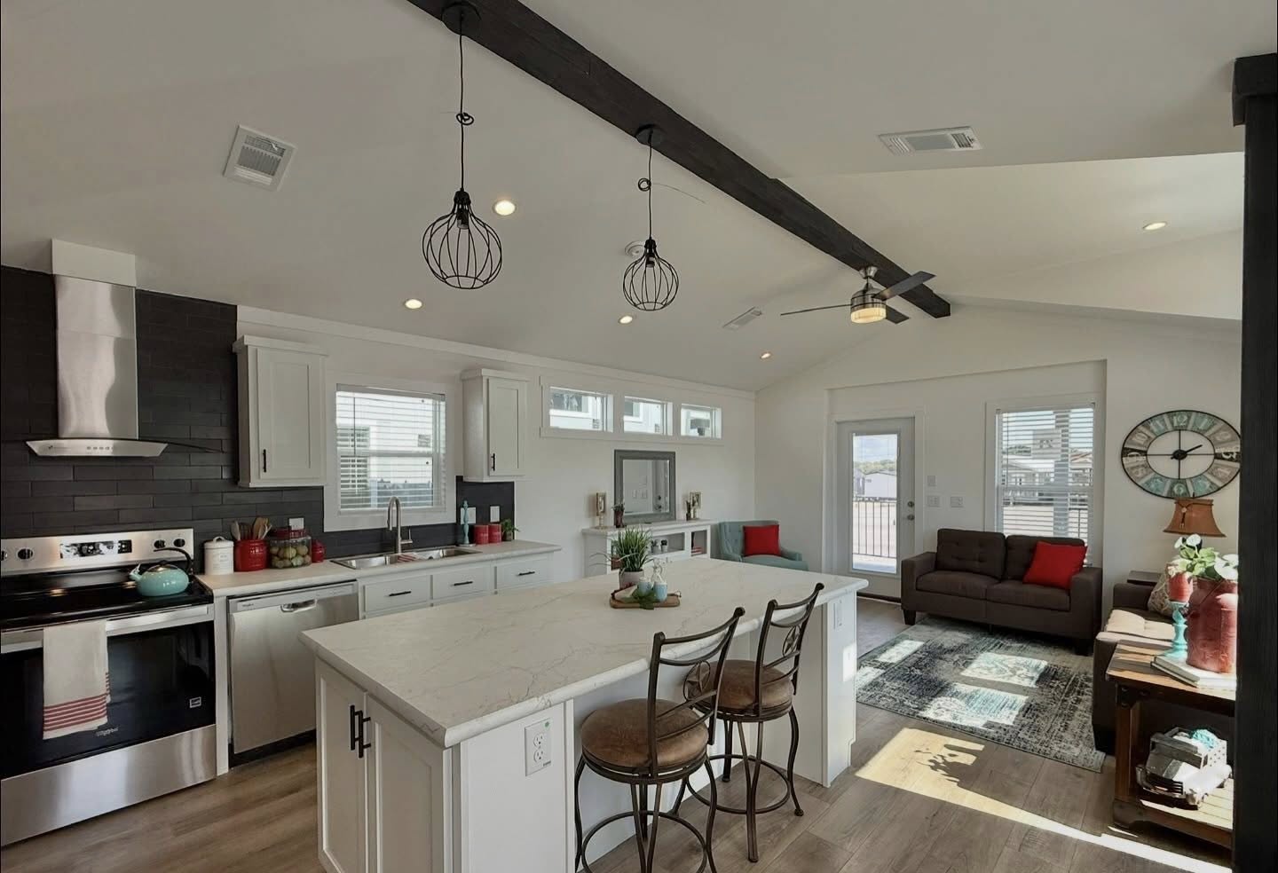 Modern kitchen and living area with exposed beams, a marble island with bar stools, sleek appliances, and a cozy seating area. Aesthetic and inviting.