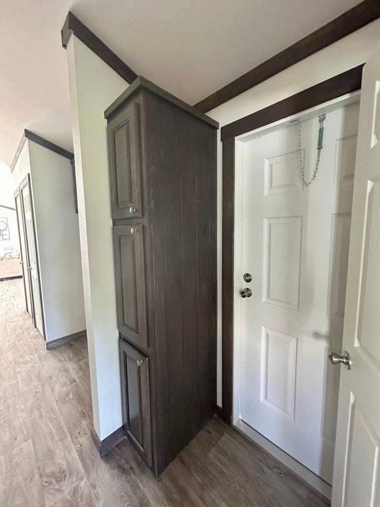 Narrow dark wooden cabinet squeezed tightly between a white wall and a closed white door with a chain lock, in a compact, modern hallway.