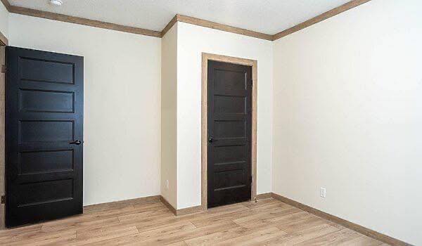 Minimalist room with light walls, wood floor, and two black doors. The space is clean, modern, and empty, conveying a calm, neutral tone.