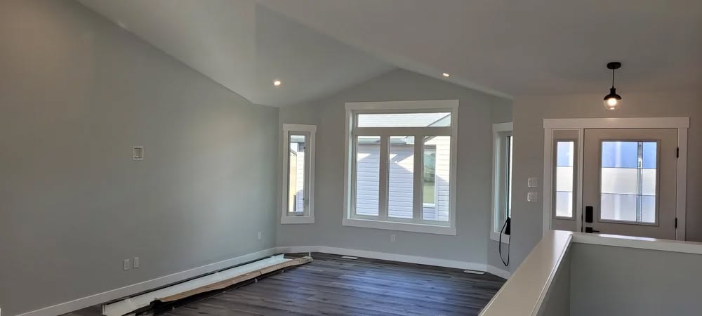 Spacious, empty room with vaulted ceiling, large windows, light gray walls, and dark wood flooring. Natural light creates an airy, calm atmosphere.