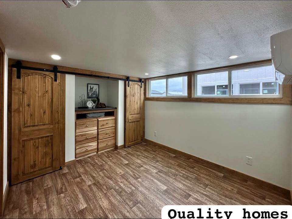 A cozy room with wooden flooring and two wooden sliding barn doors revealing shelves and drawers. Large windows let in light, creating a warm atmosphere.