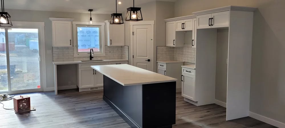 Modern kitchen with a large white island, black base, white cabinets, and gray wooden floor. Industrial pendant lights add a stylish touch.